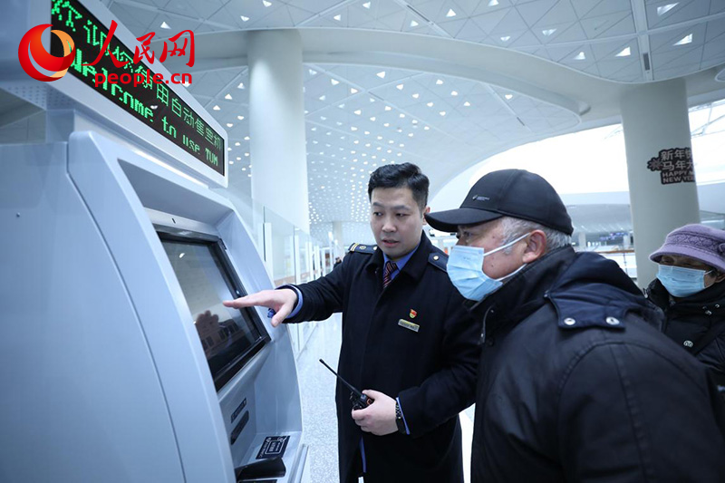 1月4日，在北京通州站，邵辰飞（左）帮助旅客使用自助购票机。人民网记者 尹星云摄